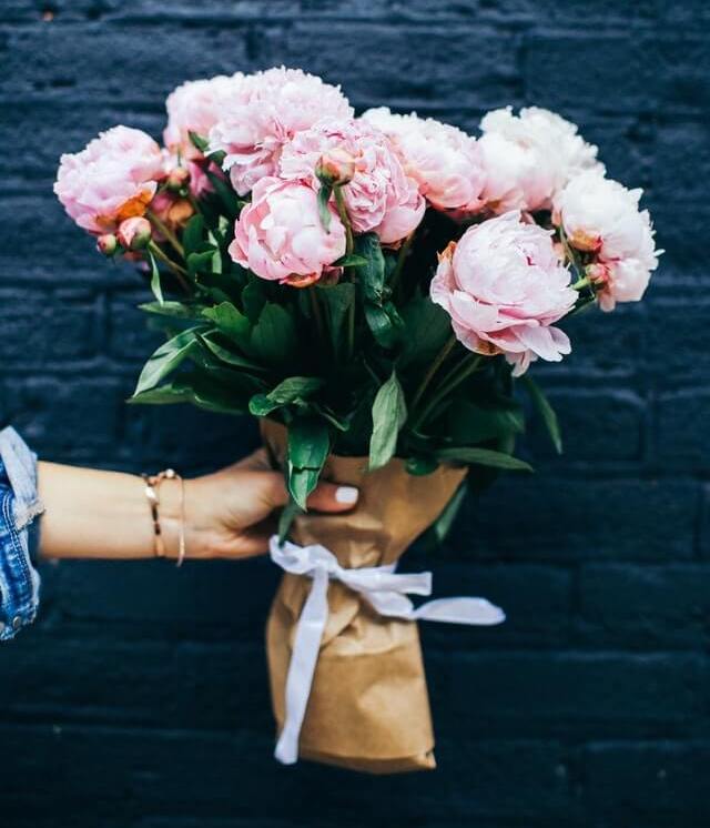 En flot buket med lyserøde blomster, som er pakket ind i gråt papir